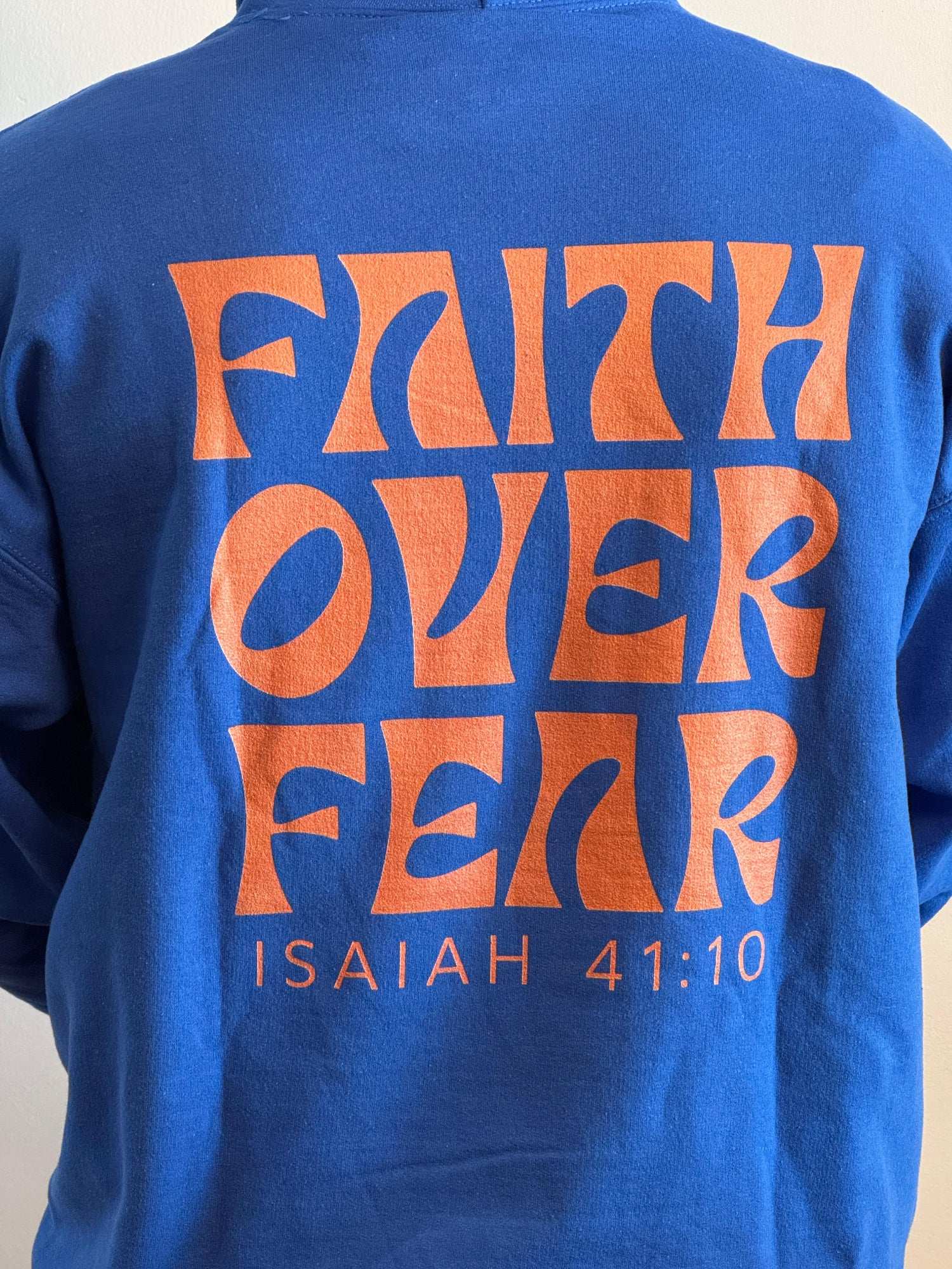 Blue sweatshirt with 'Faith Over Fear' text in orange on a plain background