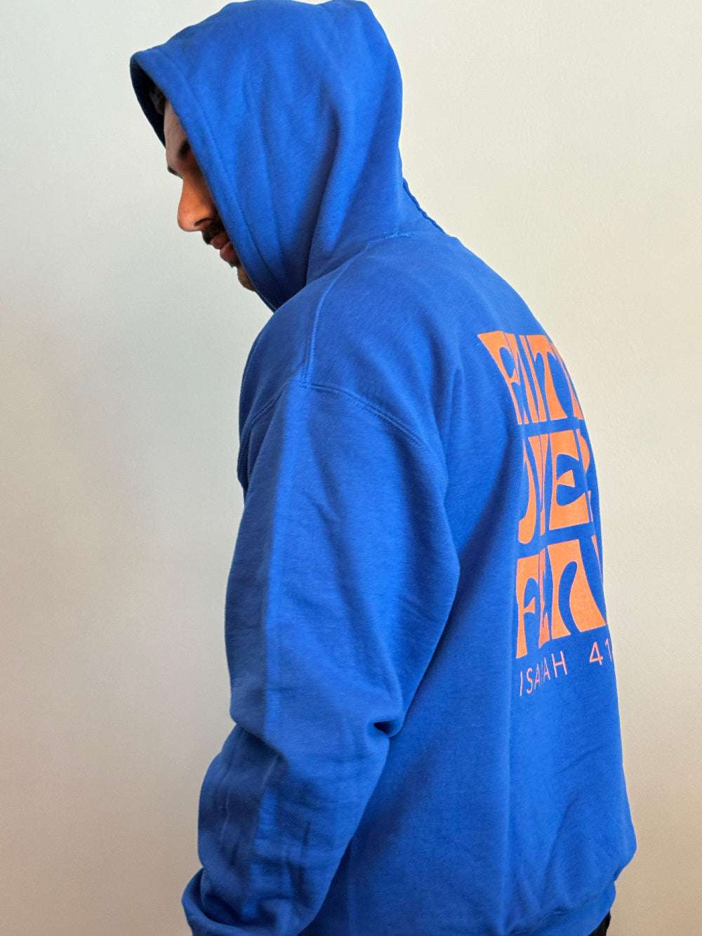 Person wearing a blue hoodie with orange text on the back against a plain background