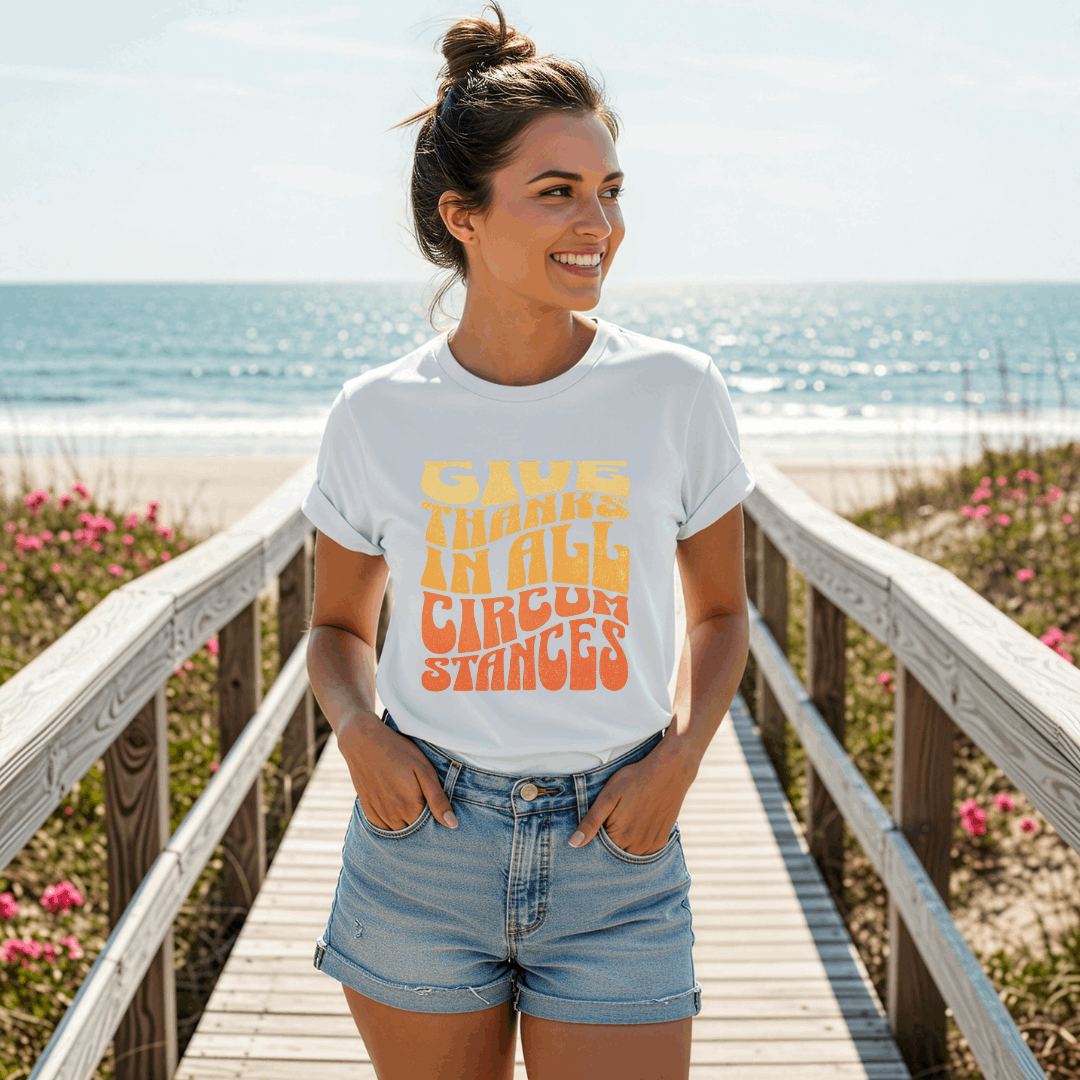 Woman wearing a white t-shirt with colorful text on a wooden boardwalk by the beach.