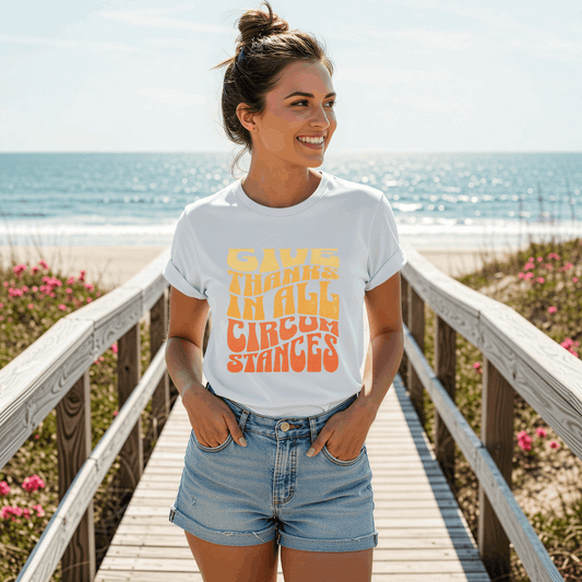 Woman wearing a white t-shirt with colorful text on a wooden boardwalk by the beach.