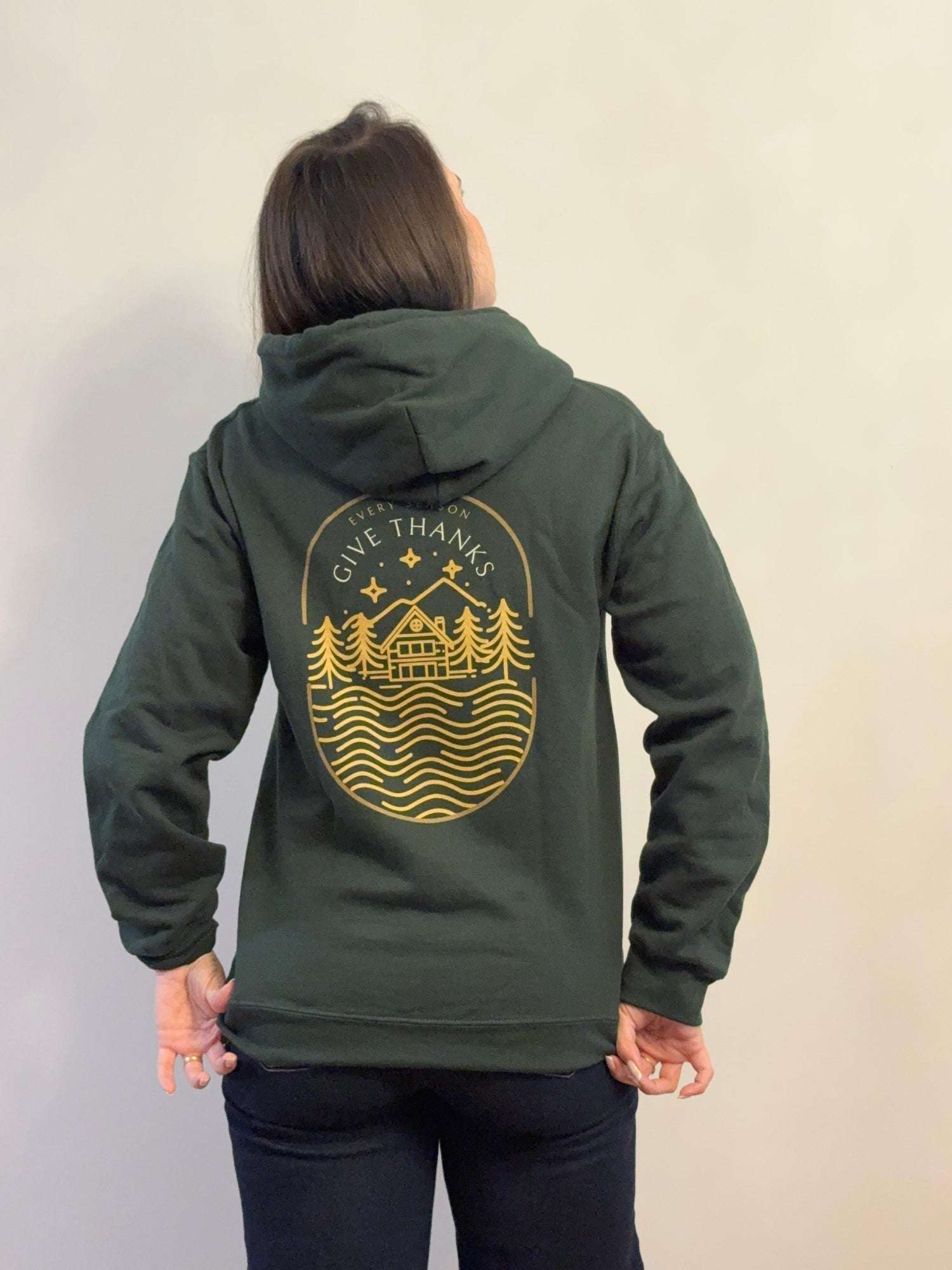 Person wearing a green hoodie with a gold graphic on the back against a plain background