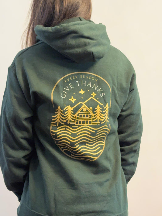 Green hoodie with gold 'Give Thanks' design on the back, worn by a person.