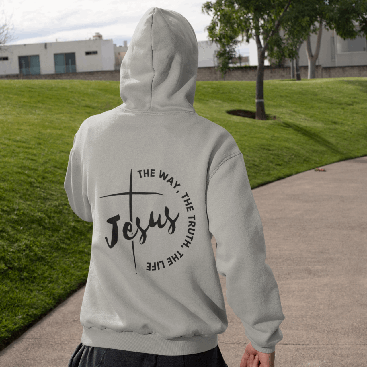 Person wearing a hoodie with 'Jesus' and cross design outdoors on a path.