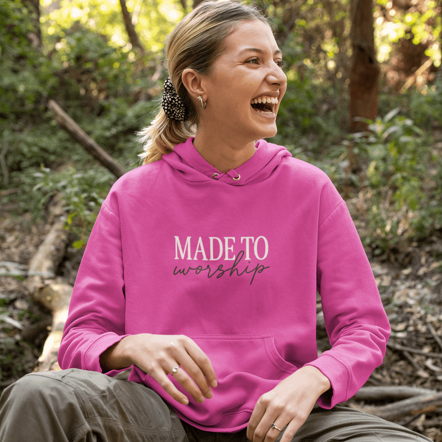 Person wearing a pink hoodie with 'MADE TO worship' text, sitting outdoors.